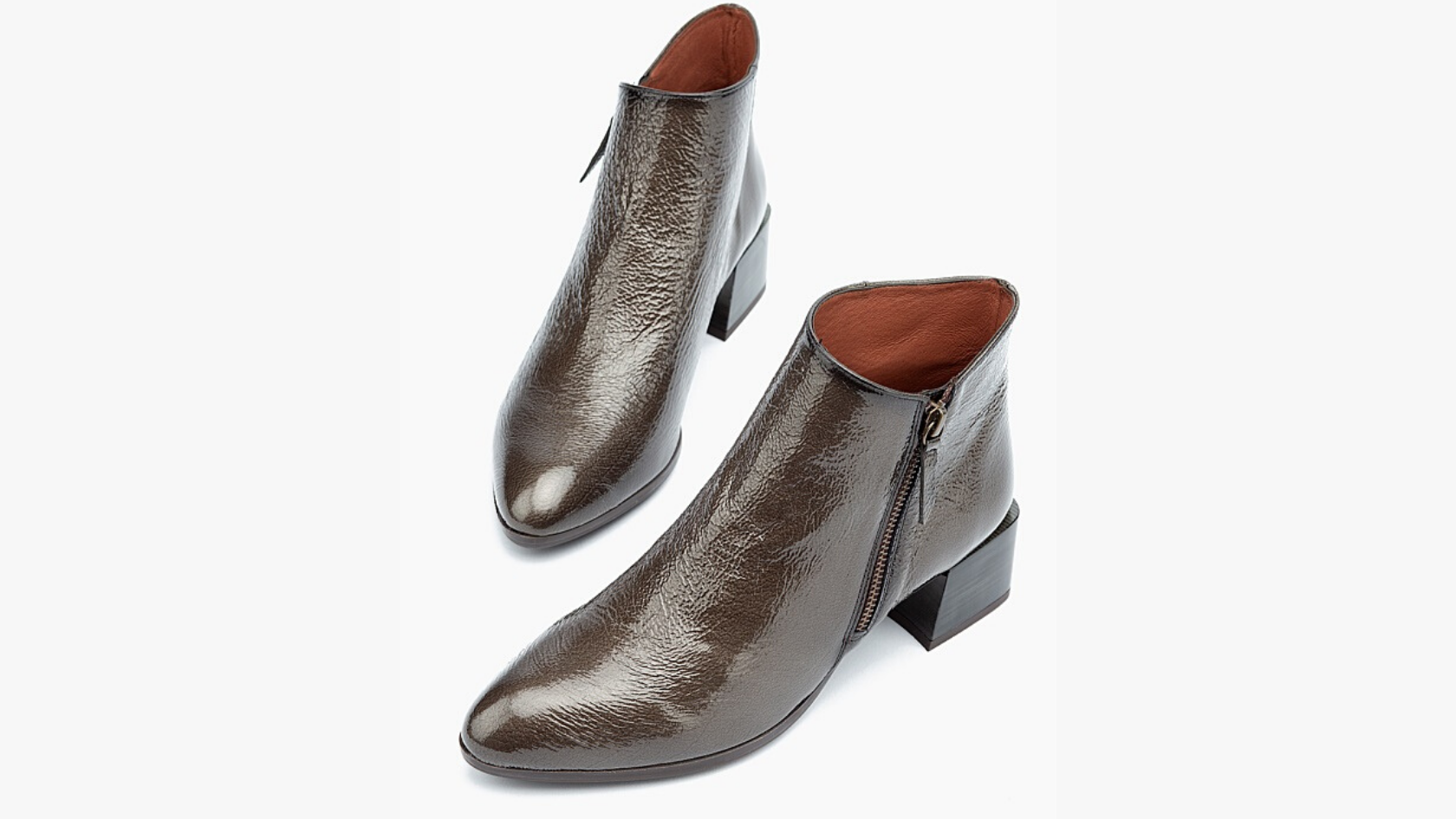 A pair of Hispanitas women’s heeled ankle boots with a taupe patent leather upper against a neutral background.   