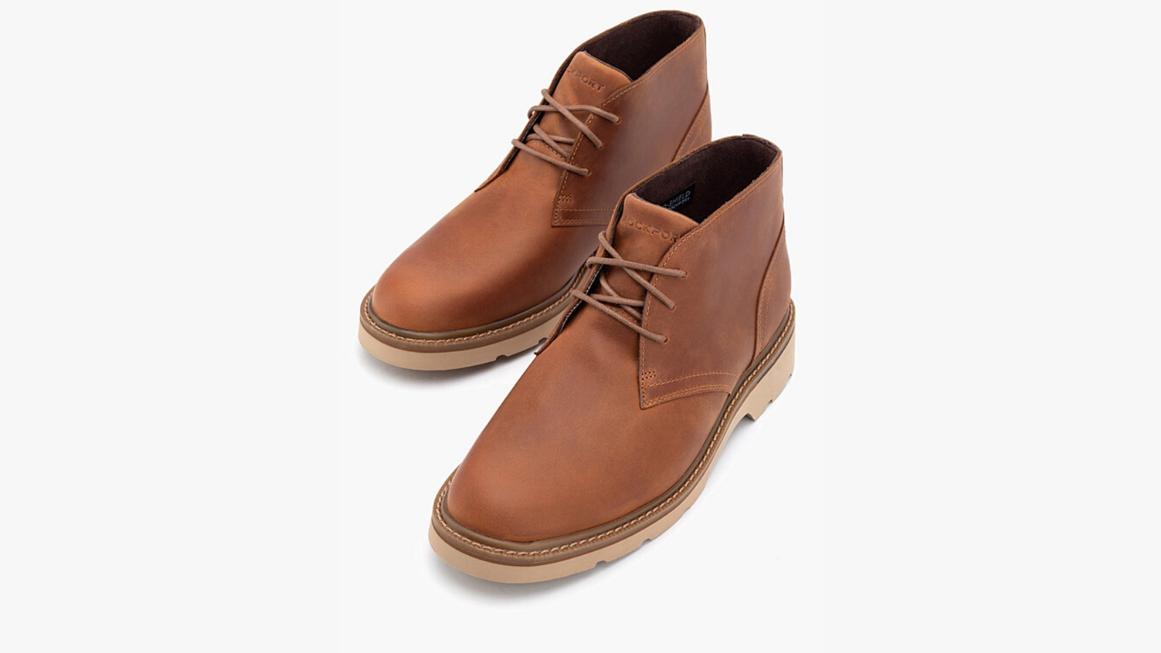 A pair of men’s Rockport tan leather lace up ankle boots against a neutral background.  