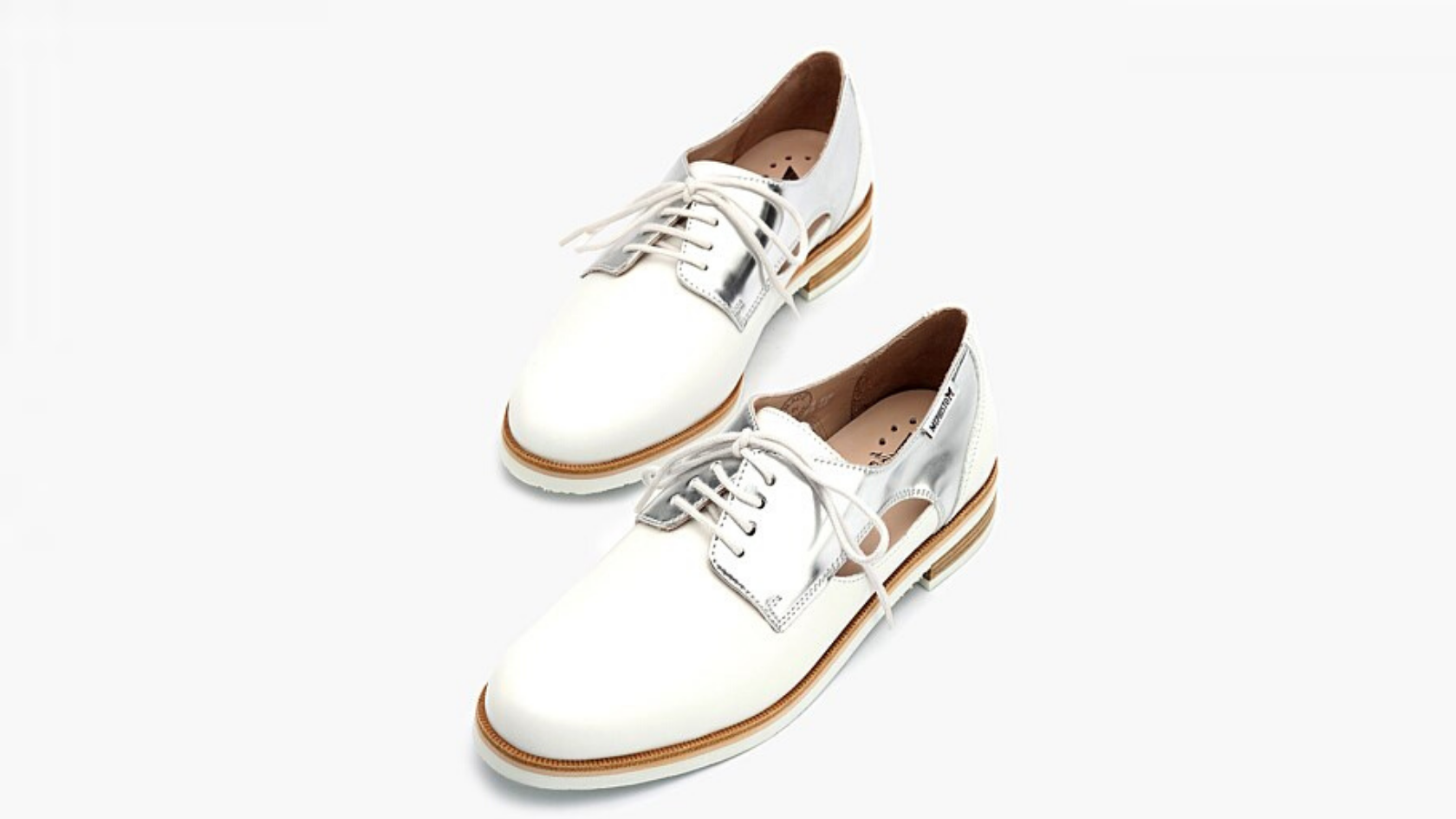 Pair of white loafers with glossy silver panelling suspended against a neutral background.
